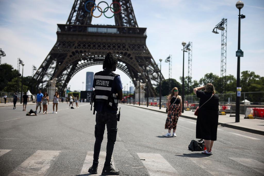 A security officer watches people taking photographs in front of the Eiffel Tower ahead of the 2024 Summer Olympics